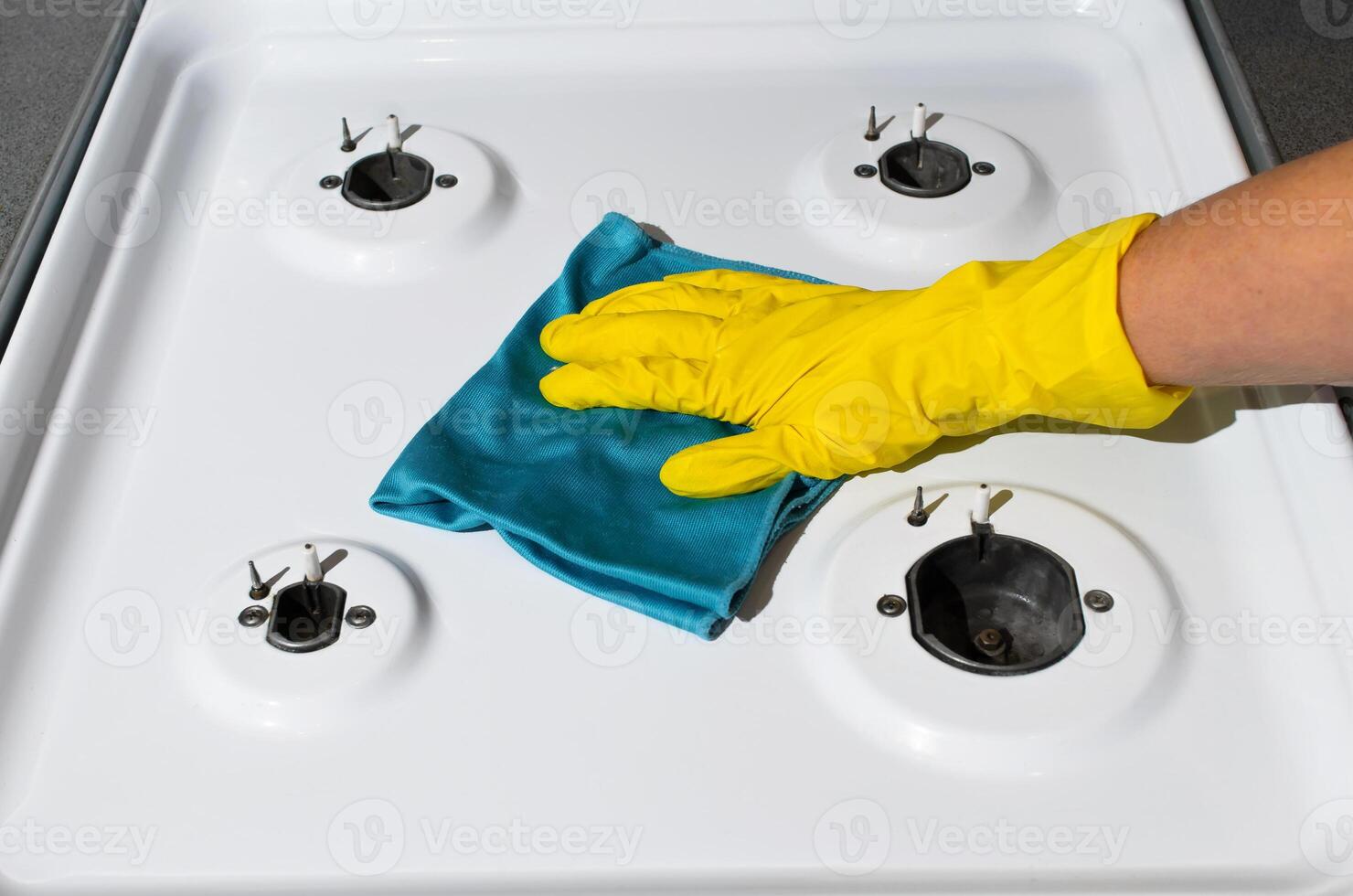 Woman washing gas stove, close-up. Woman's hand in glove wipes the gas panel with rag. Cleaning of kitchen apartments photo