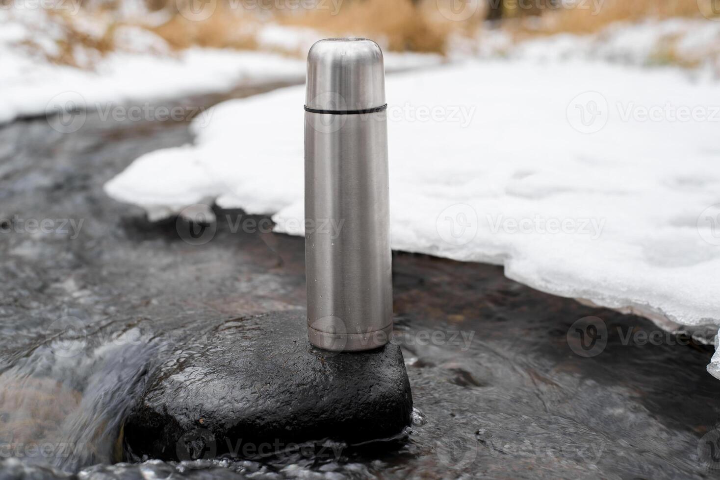 Vacuum thermos standing in the stream. Camping thermos outside in winter, close-up. Adventure, hike, travel concept. photo