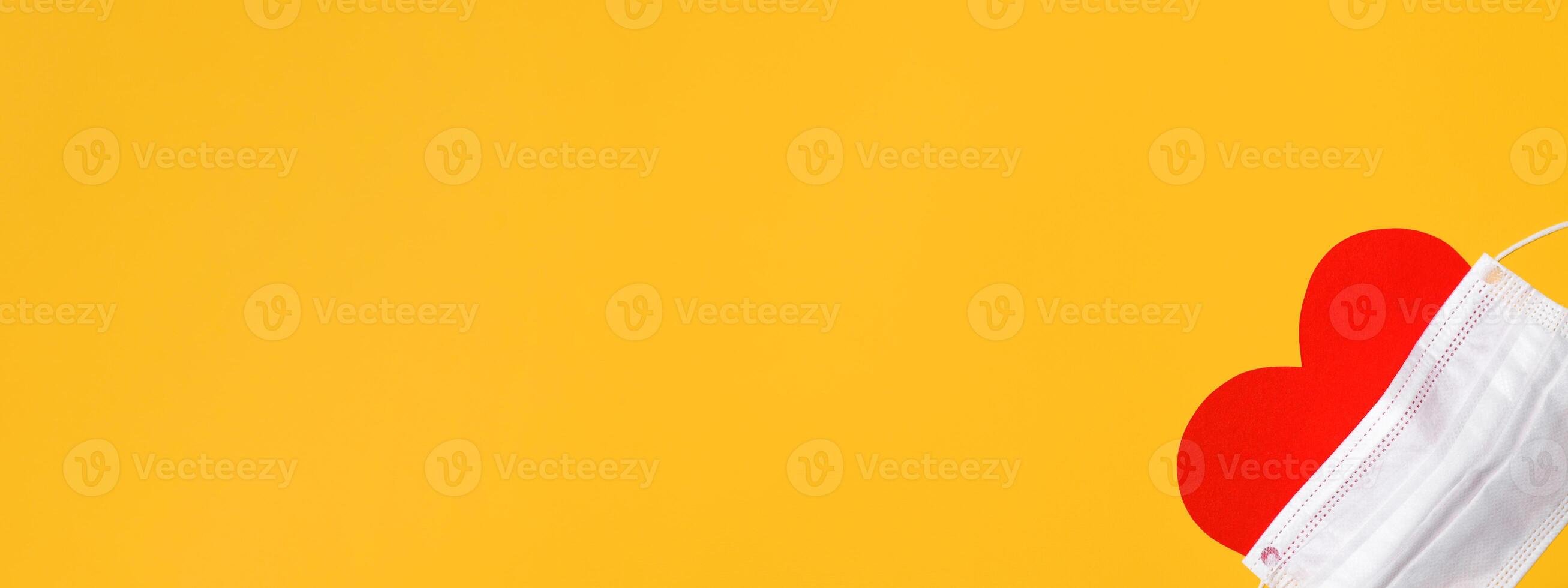 Red heart in a medical mask on a yellow background, flat lay. Conceptual banner, copy space. photo