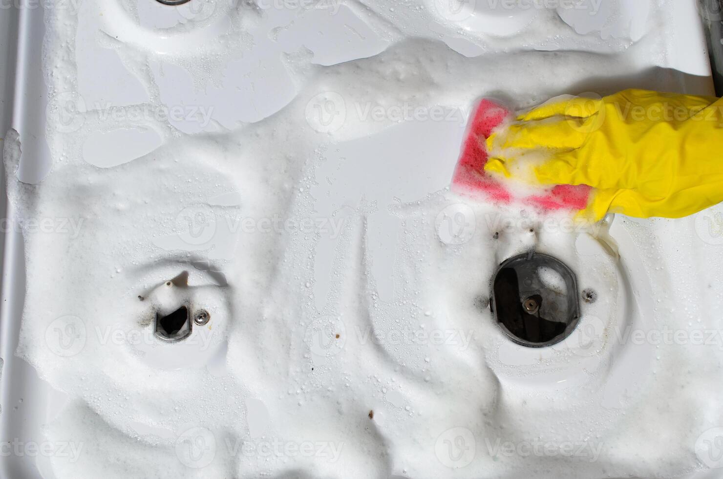 Woman cleans gas stove, top view.. Female hand in glove washing gas panel with sponge. Hygienic kitchen cleaning photo