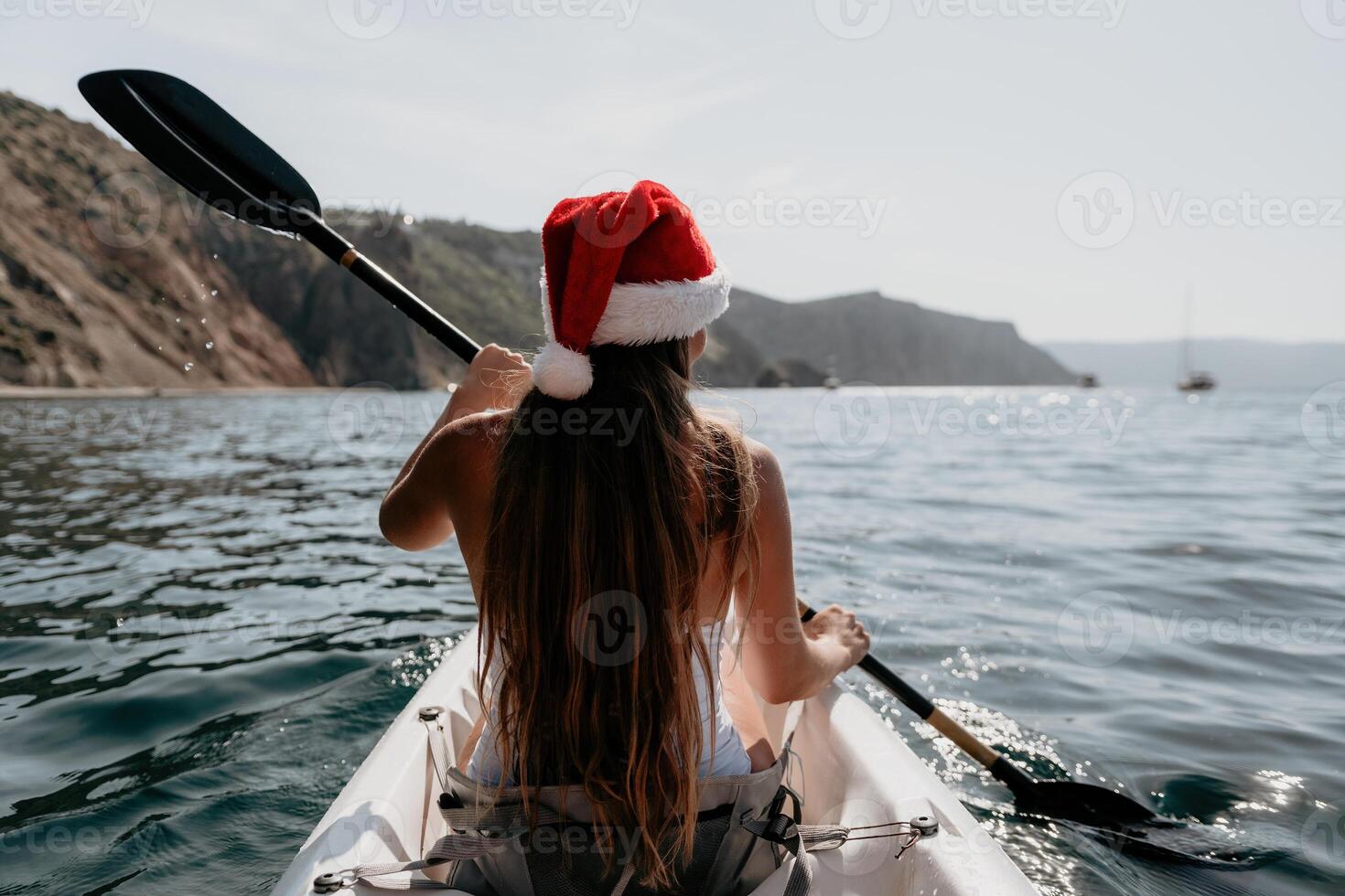 Woman in kayak back view. Happy young woman in Santa hat floating in kayak on calm sea. Summer holiday vacation and cheerful female people relaxing having fun on the boat. photo