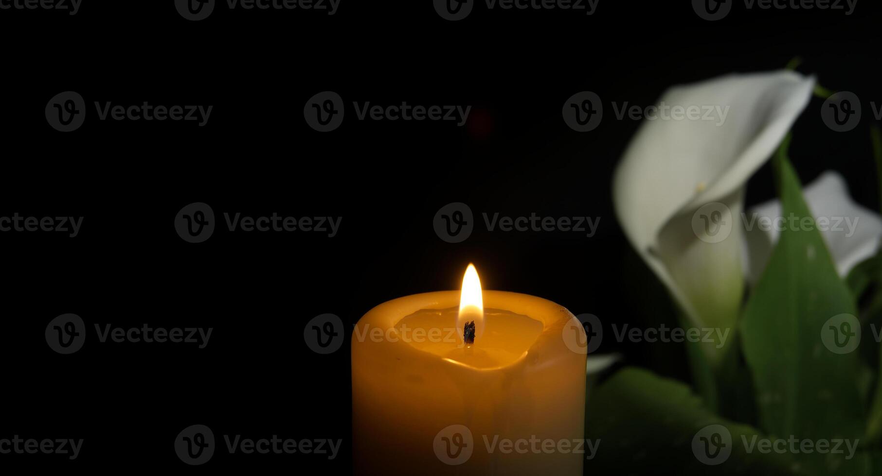 Burning wax candle and white calla lily flowers in darkness photo