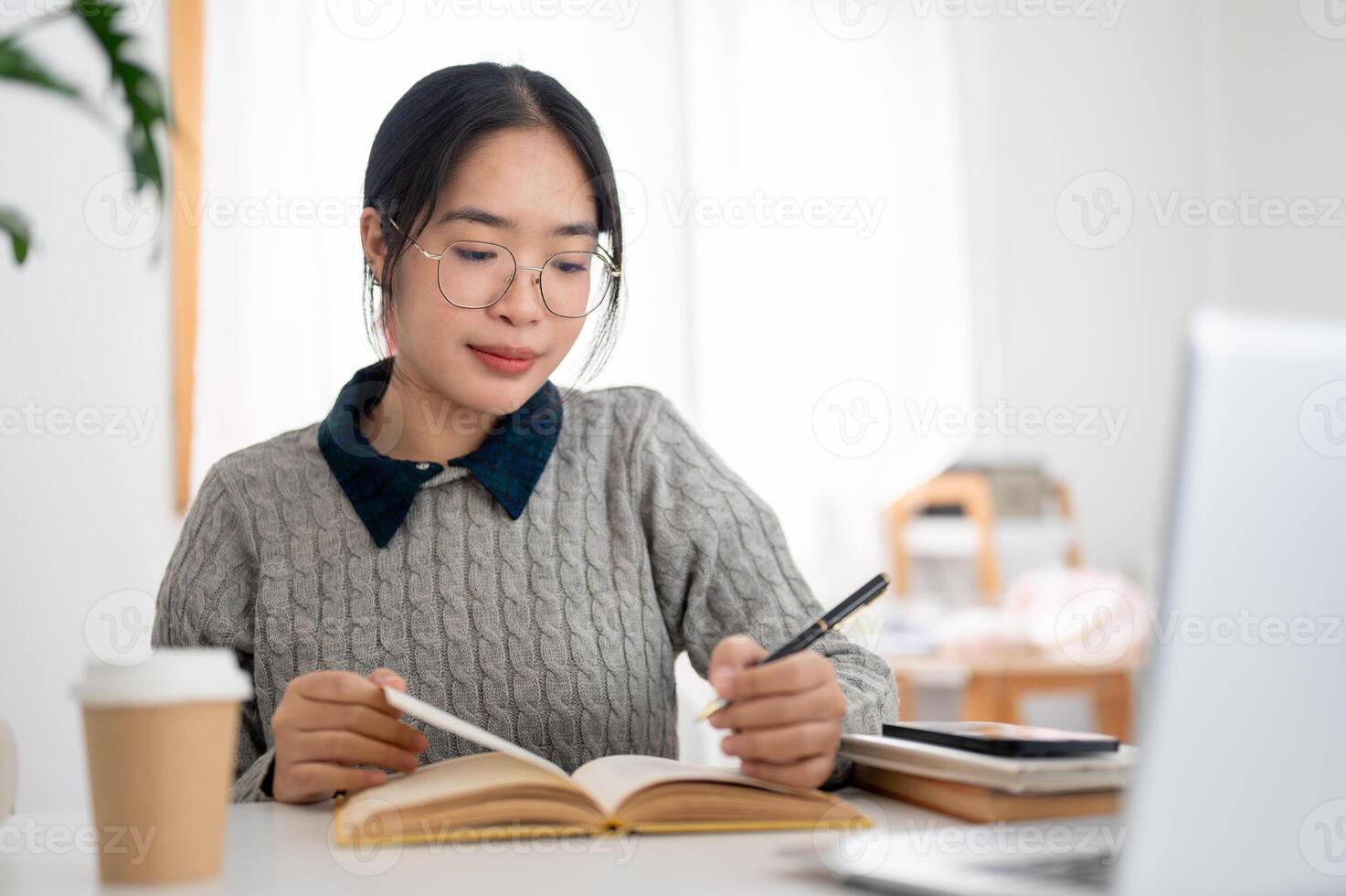 A young Asian female student is focusing on her homework and reading book at a table in her room. photo