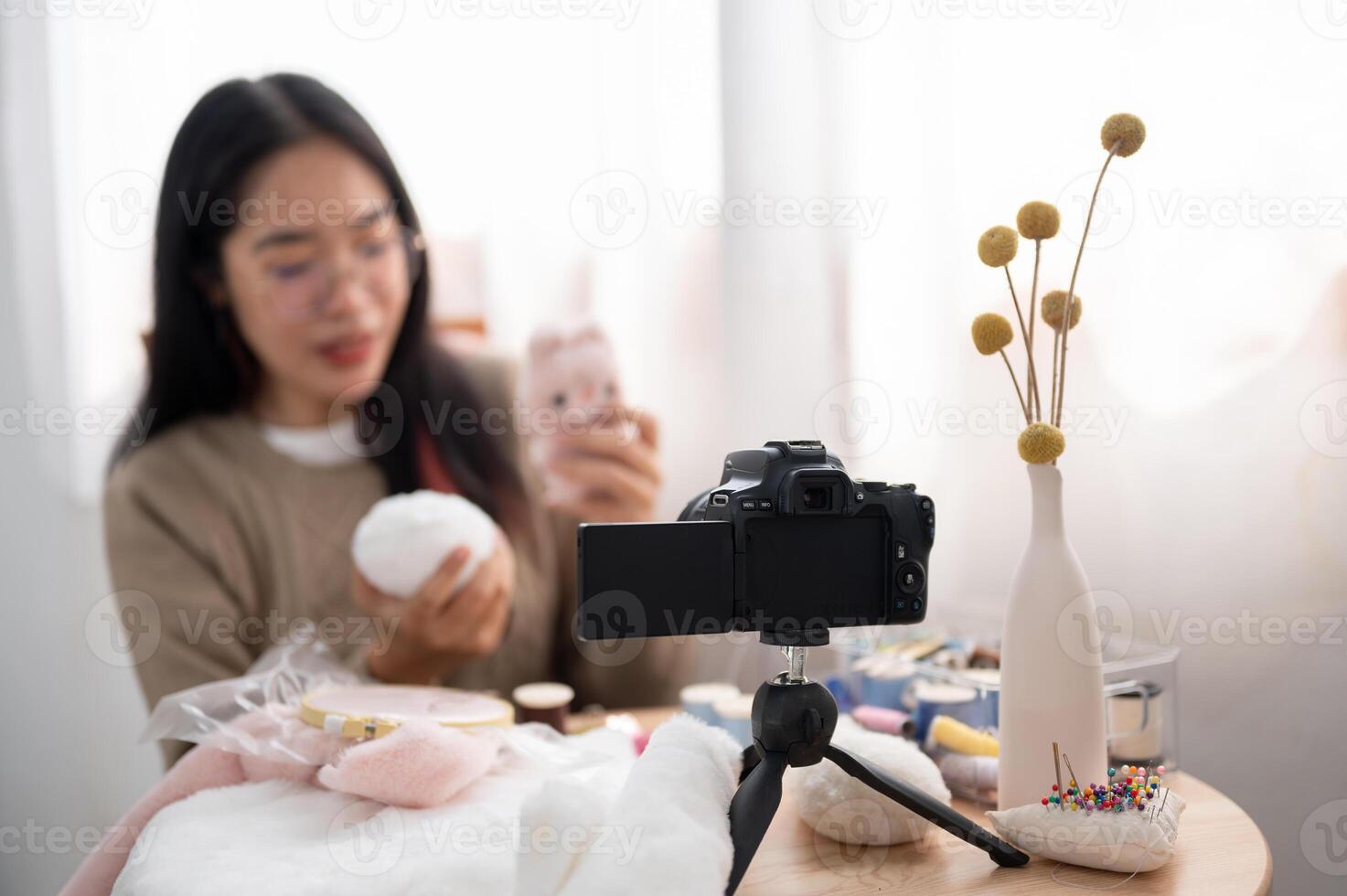 A smiling Asian female content creator is talking with the camera, showing her handmade plushie. photo