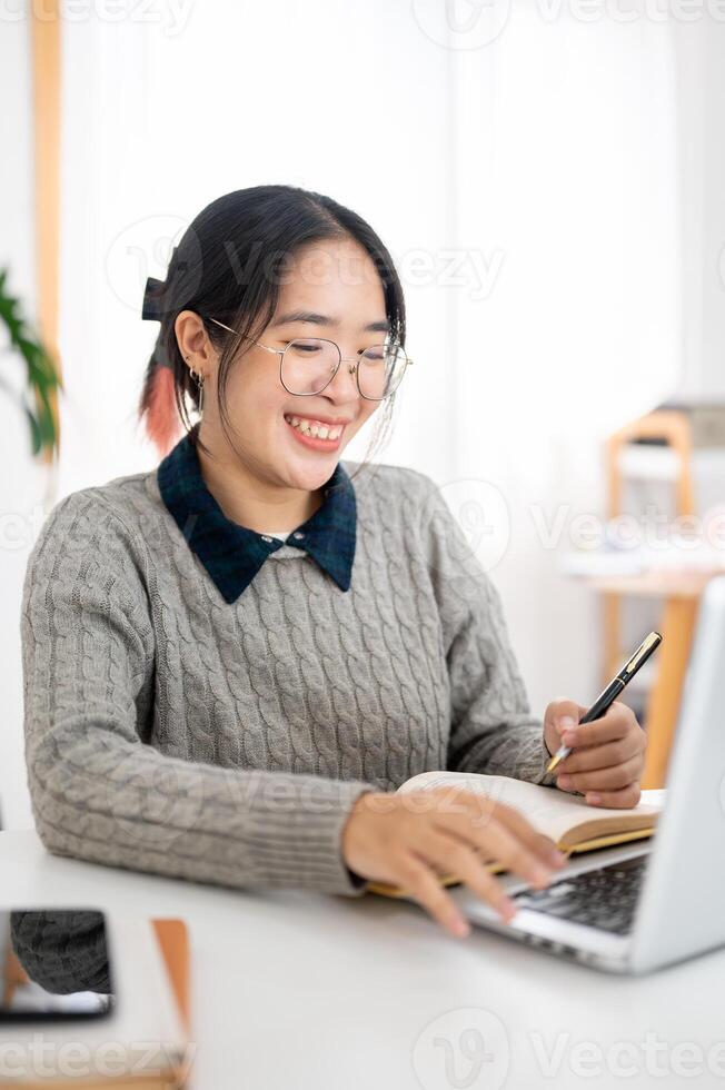 A cheerful young Asian female college student is studying online in a cafe co-working space. photo