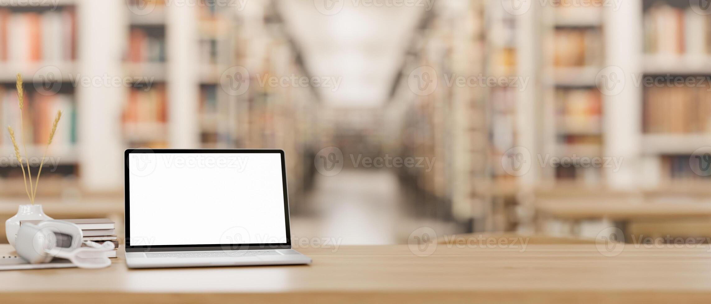 A wooden table features a white-screen laptop computer mockup in a spacious library. photo