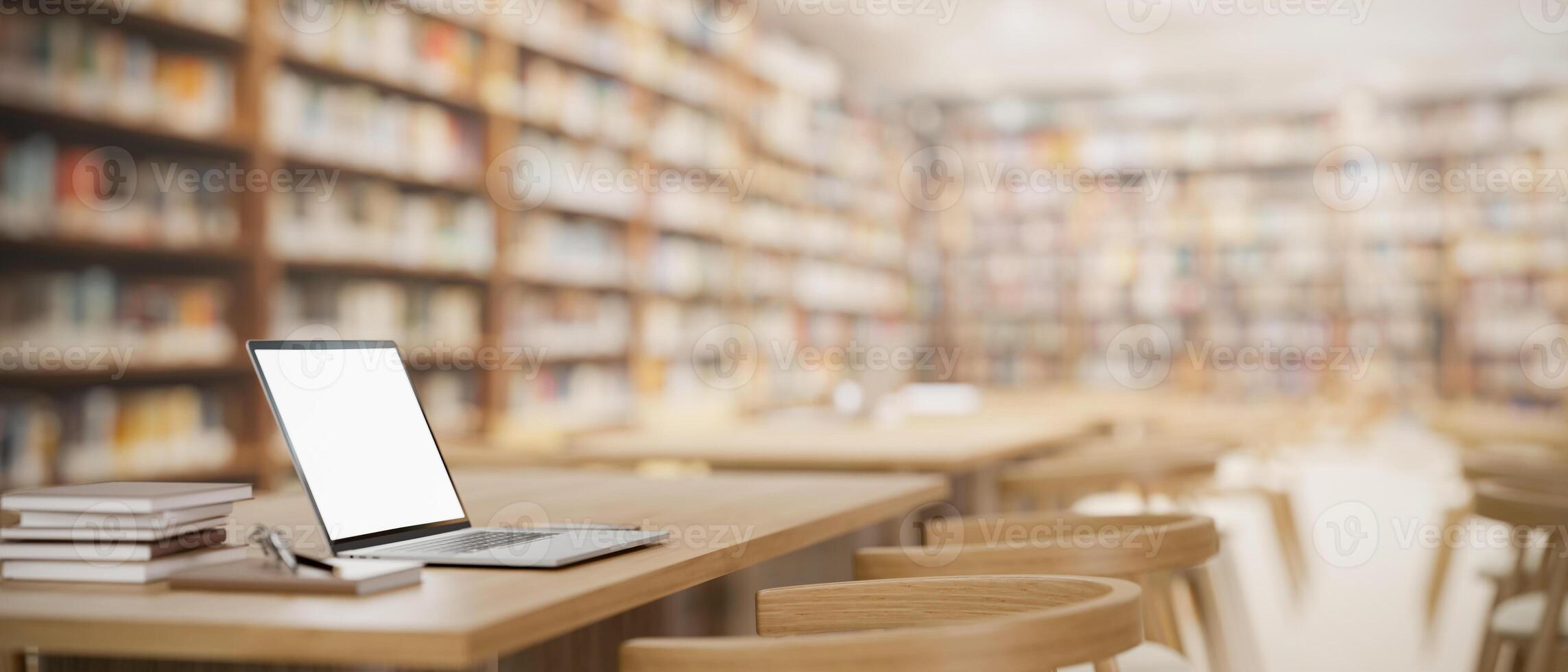 A white-screen laptop computer mockup and books on a wooden table in a spacious university library. photo