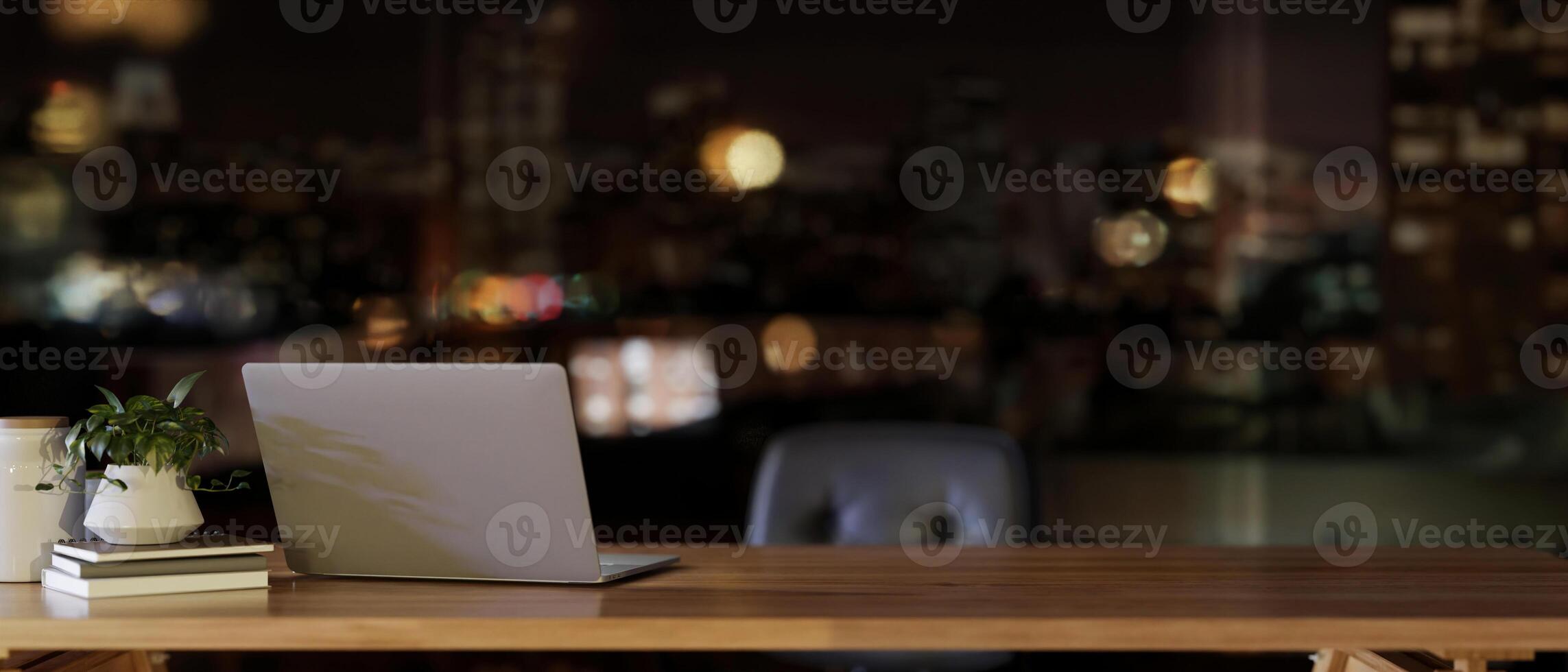 A laptop computer on a wooden desk in a modern office on a skyscraper at night with night city view. photo