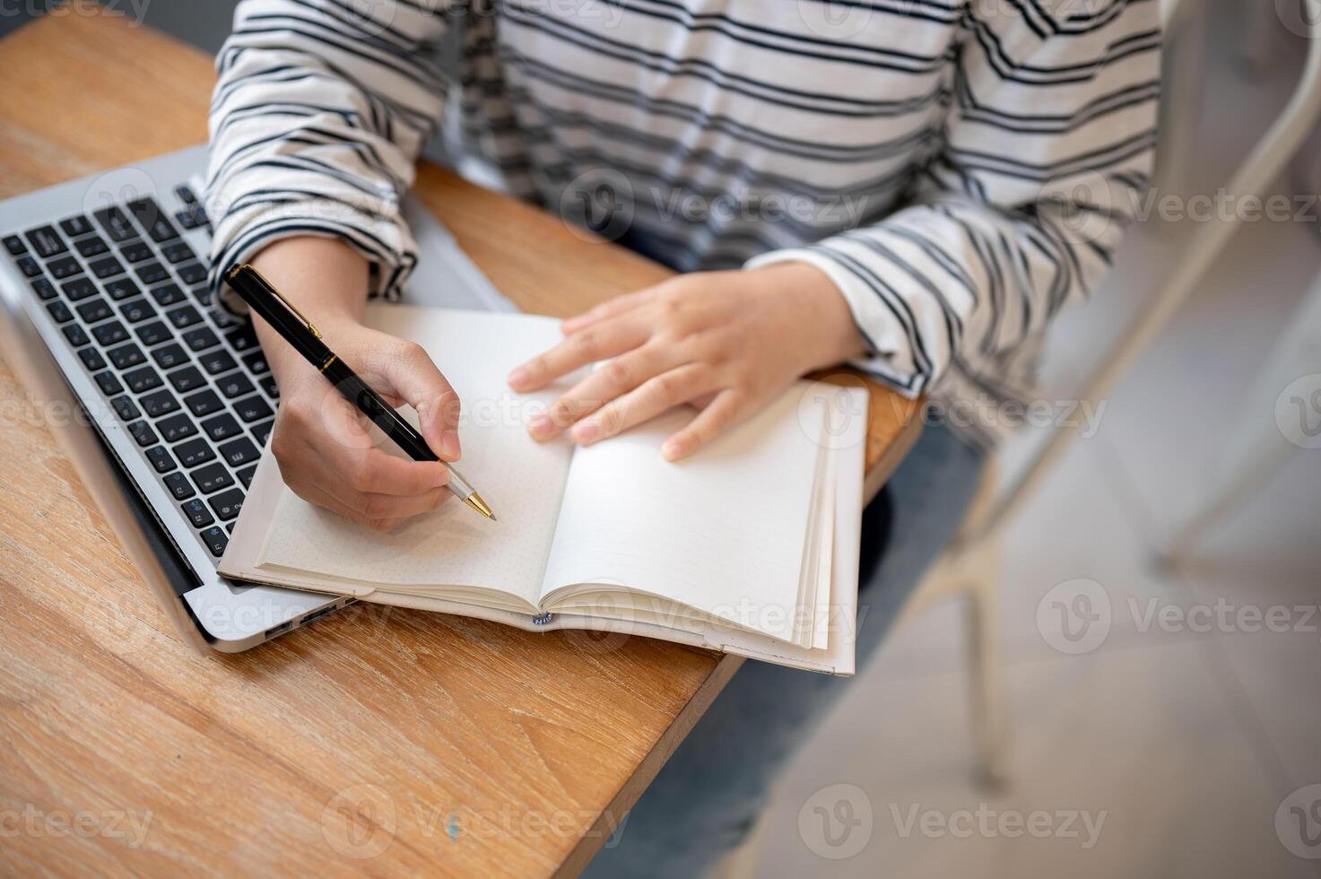 A cropped shot of a female student doing homework or taking notes in her notebook at a table. photo