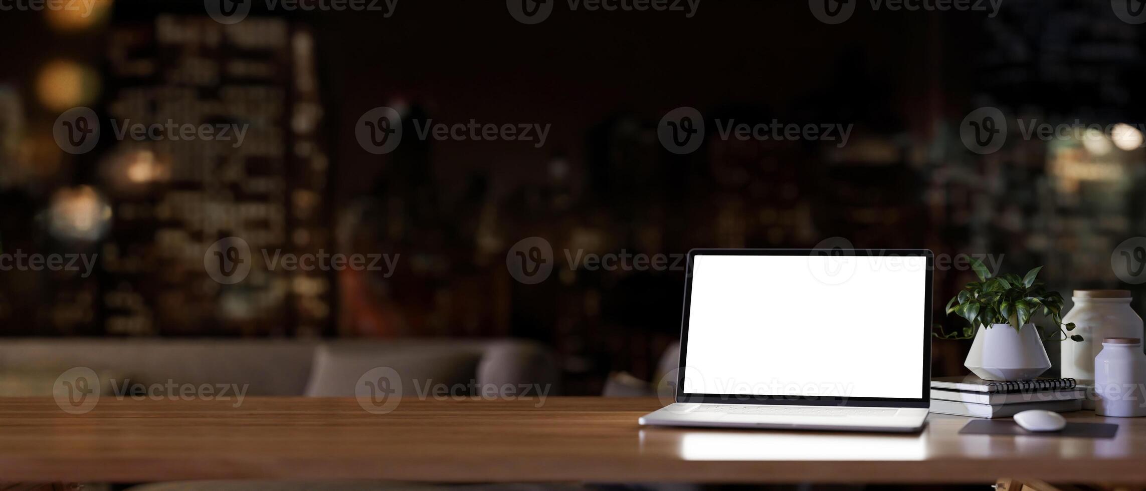 A white screen laptop computer on a wooden desk in a modern dark living room at night. photo