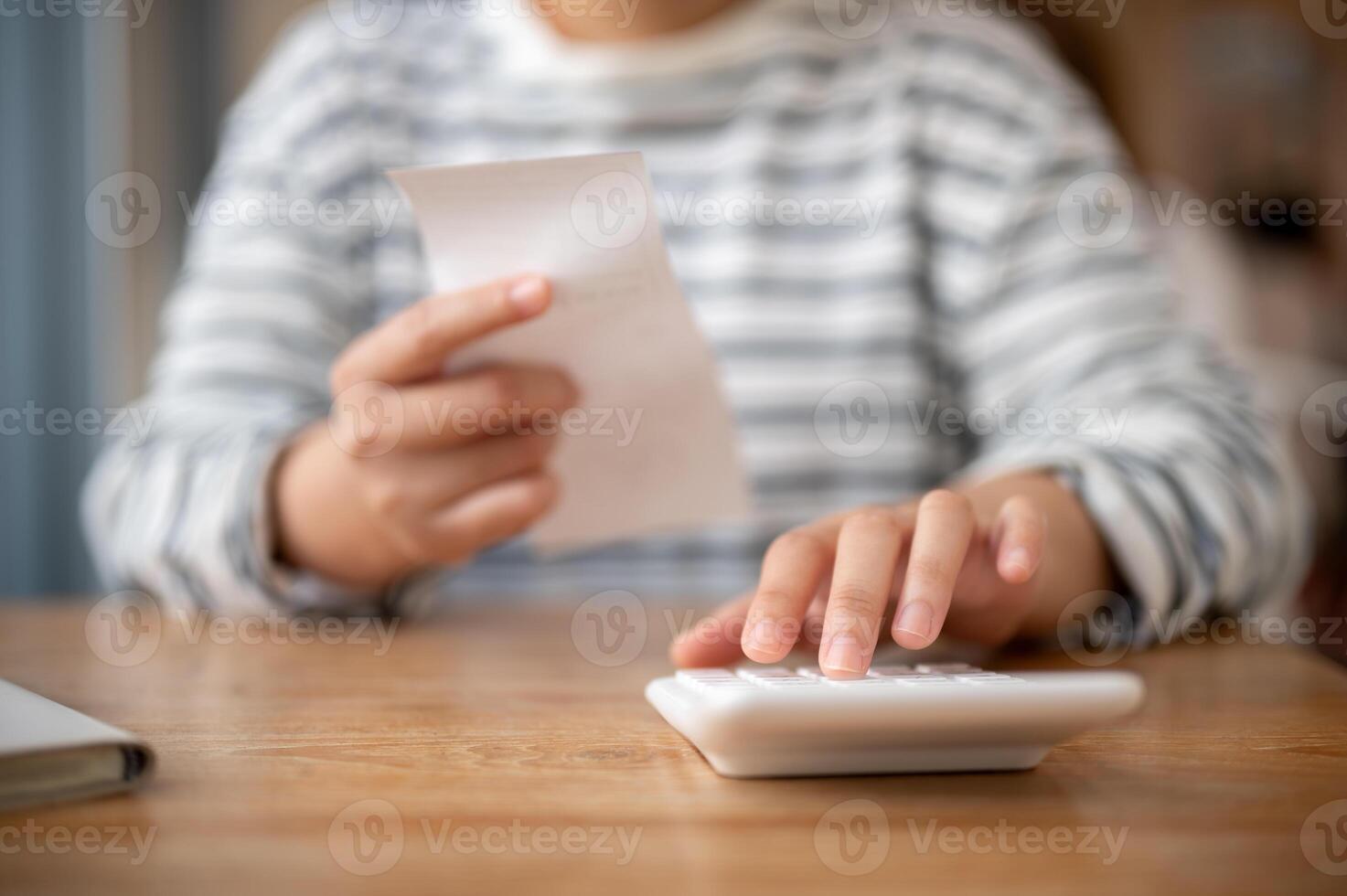 A woman using a calculator at a table, calculating her household expenses and bills. photo