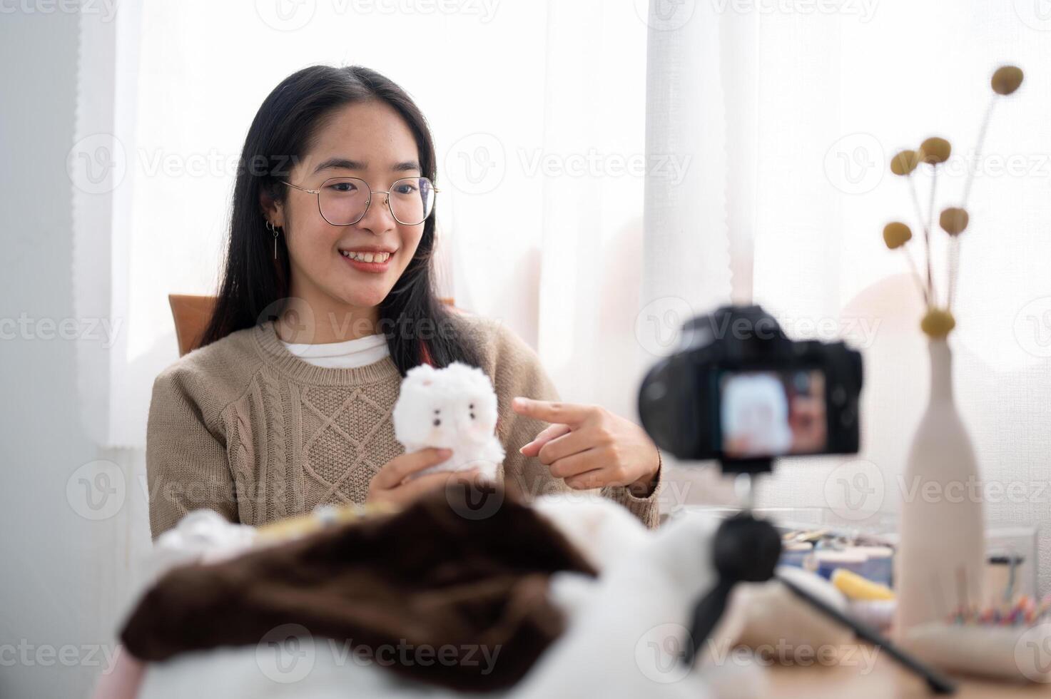A cheerful young Asian female content creator showing her cute handmade plushie to the camera. photo