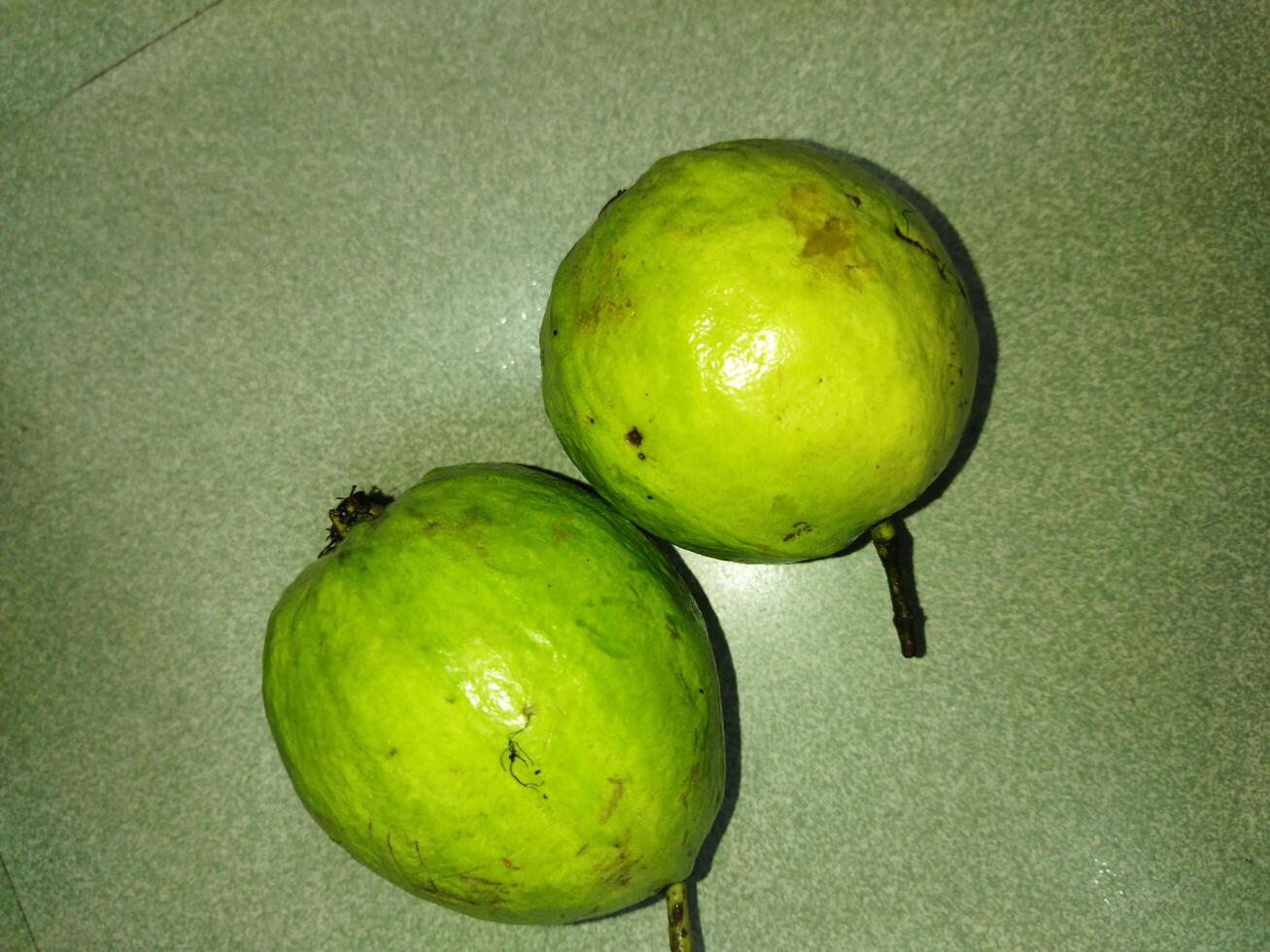 two green fruits sit on a green surface photo