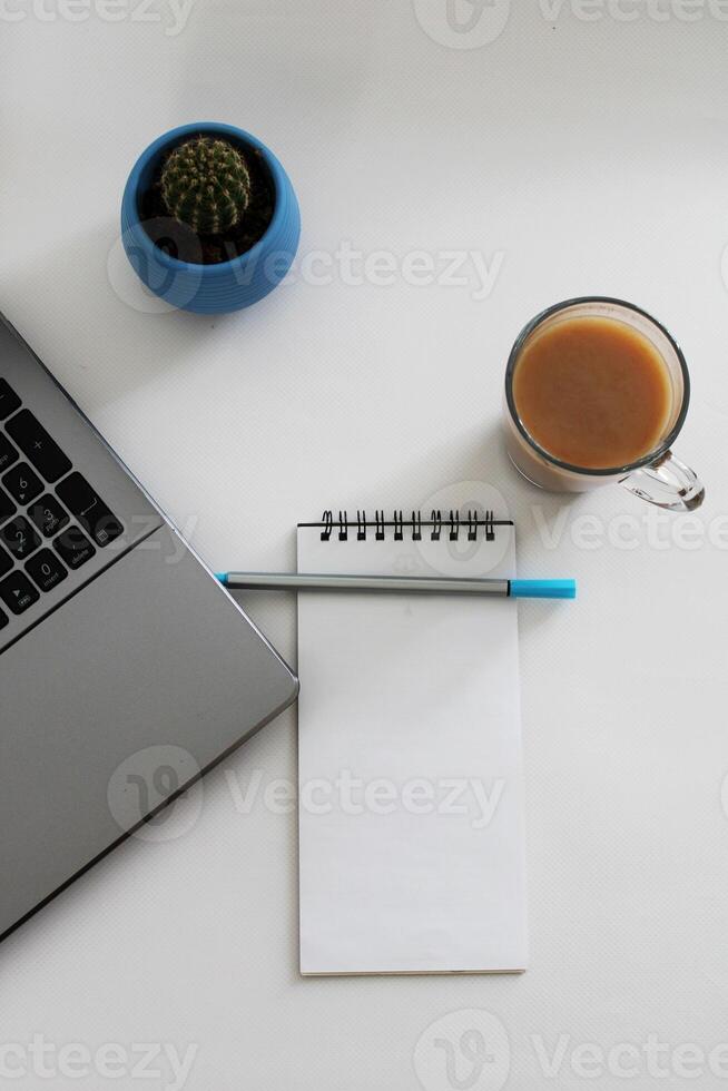 Blank notebook with pen are on top of wood office desk table with a cup of coffee and office supplies, top view. photo