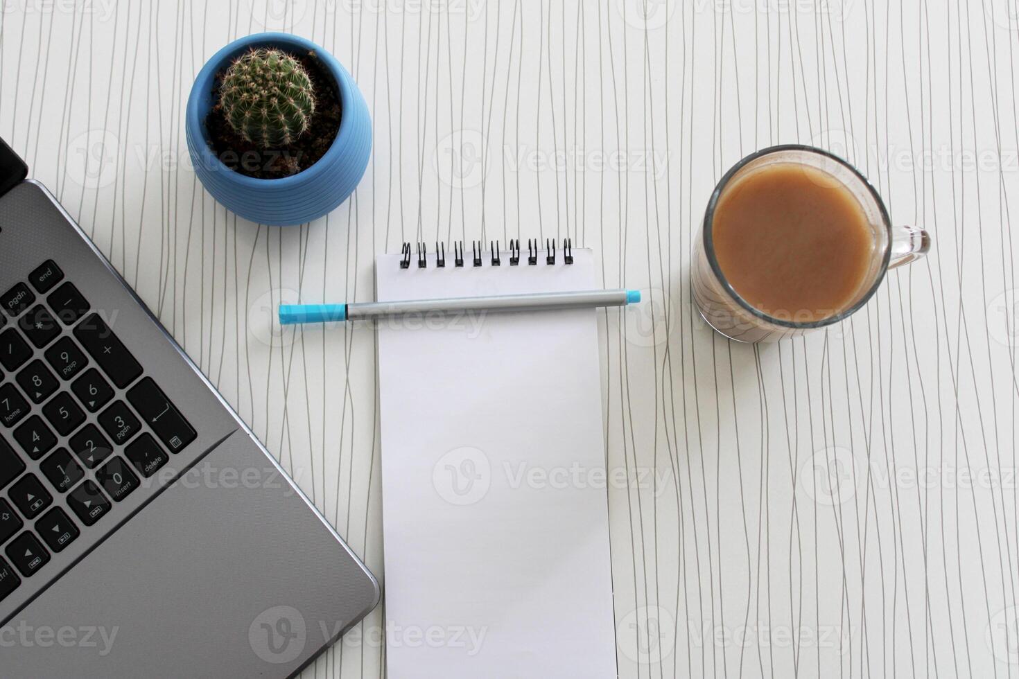 Blank notebook with pen are on top of wood office desk table with a cup of coffee and office supplies, top view. photo