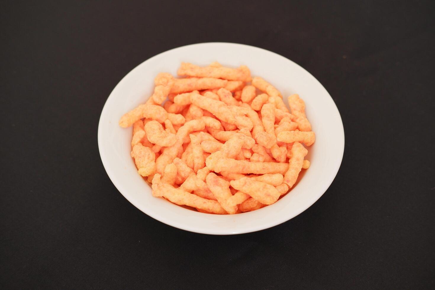 Crispy Corn Puffs in white bowl on black background. Selective focus. photo