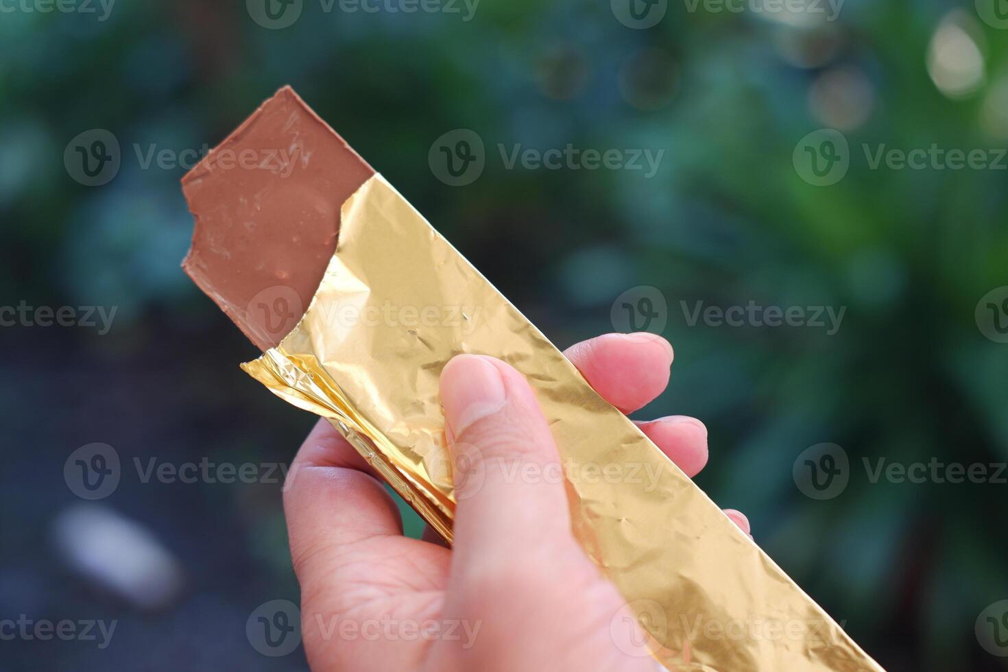 Hand holding a chocolate bar in the garden. Selective focus. photo
