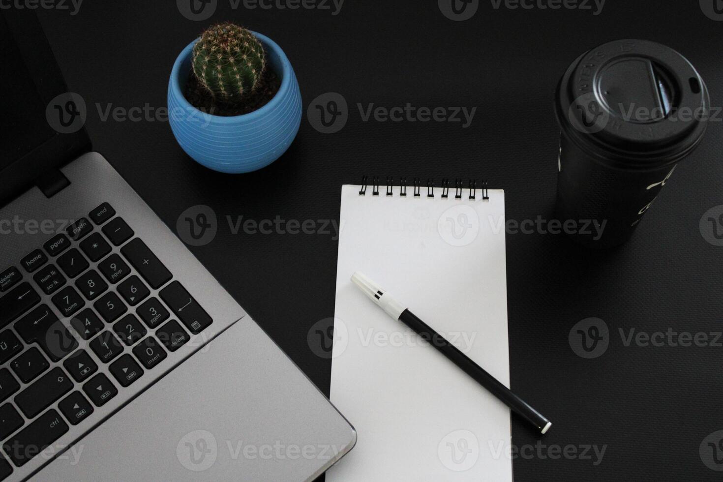 Blank notebook with pen are on top of wood office desk table with a cup of coffee and office supplies, top view. photo
