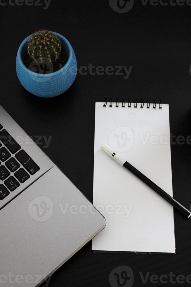 Blank notebook with pen are on top of wood office desk table with a cup of coffee and office supplies, top view. photo