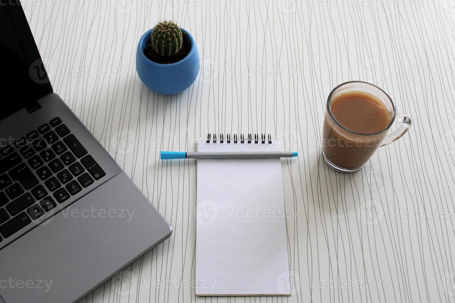 Blank notebook with pen are on top of wood office desk table with a cup of coffee and office supplies, top view. photo