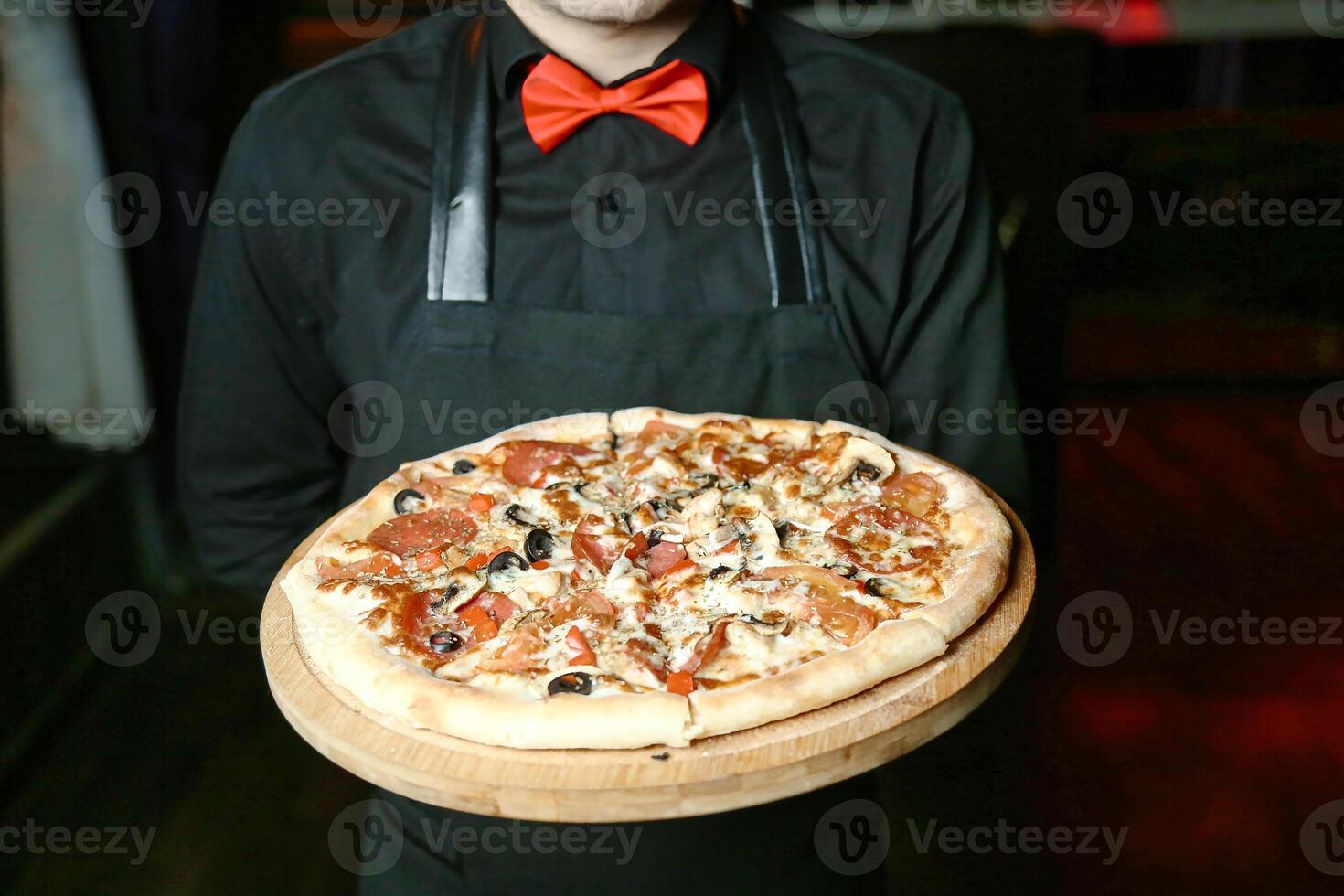 sonriente hombre en delantal participación un recién horneado Pizza foto