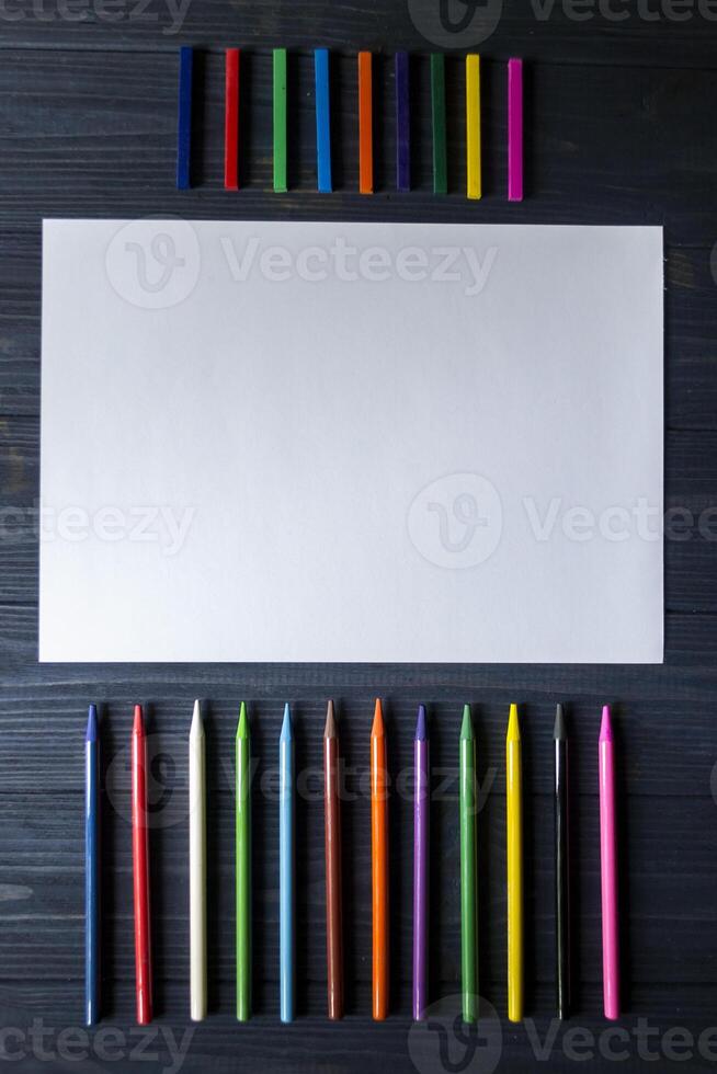 Palette of multicolored pencils and the sheet of white paper on dark blue wooden desk. photo