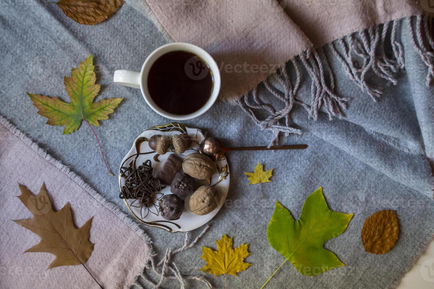 A cup of tea and sweet snacks with decoration by autumn leaves on the warm plaid. Seasonal still life photo