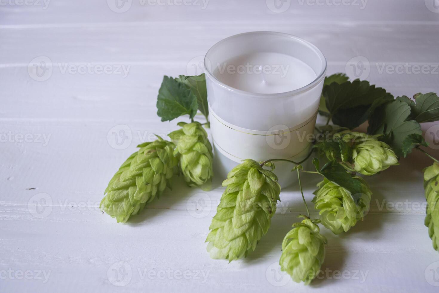 A white aroma candle and the branch of hops as decoration on a white wooden table. photo