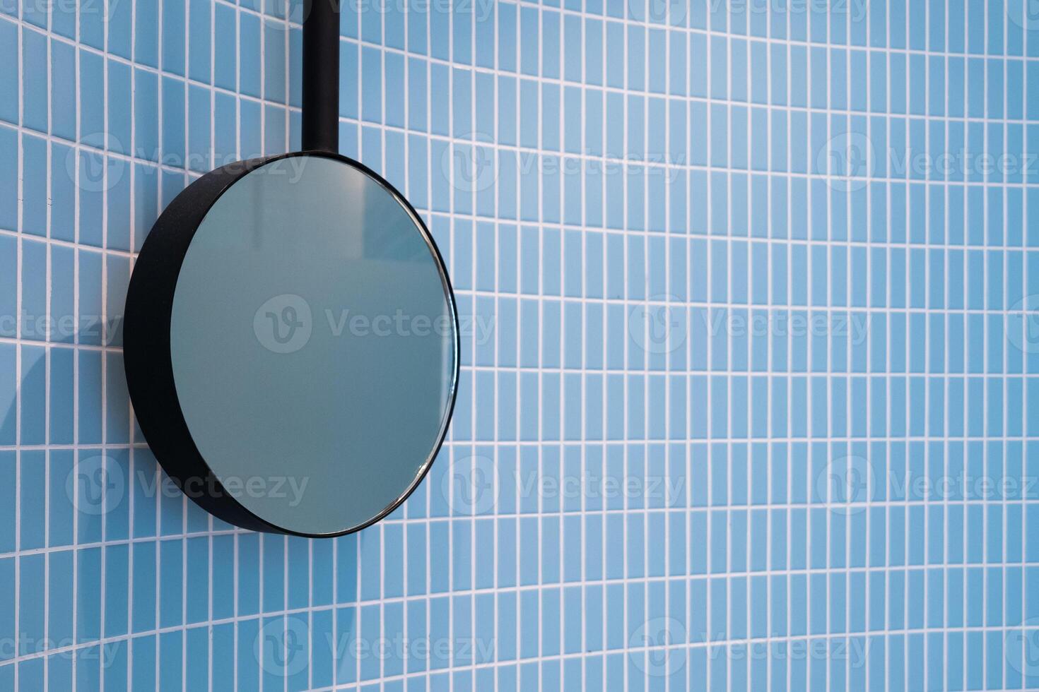 Minimalist round mirror black frame hang on a wall of ceramic baby blue tiles soft color embodying contemporary interior design simplicity pattern textured in the bathroom photo