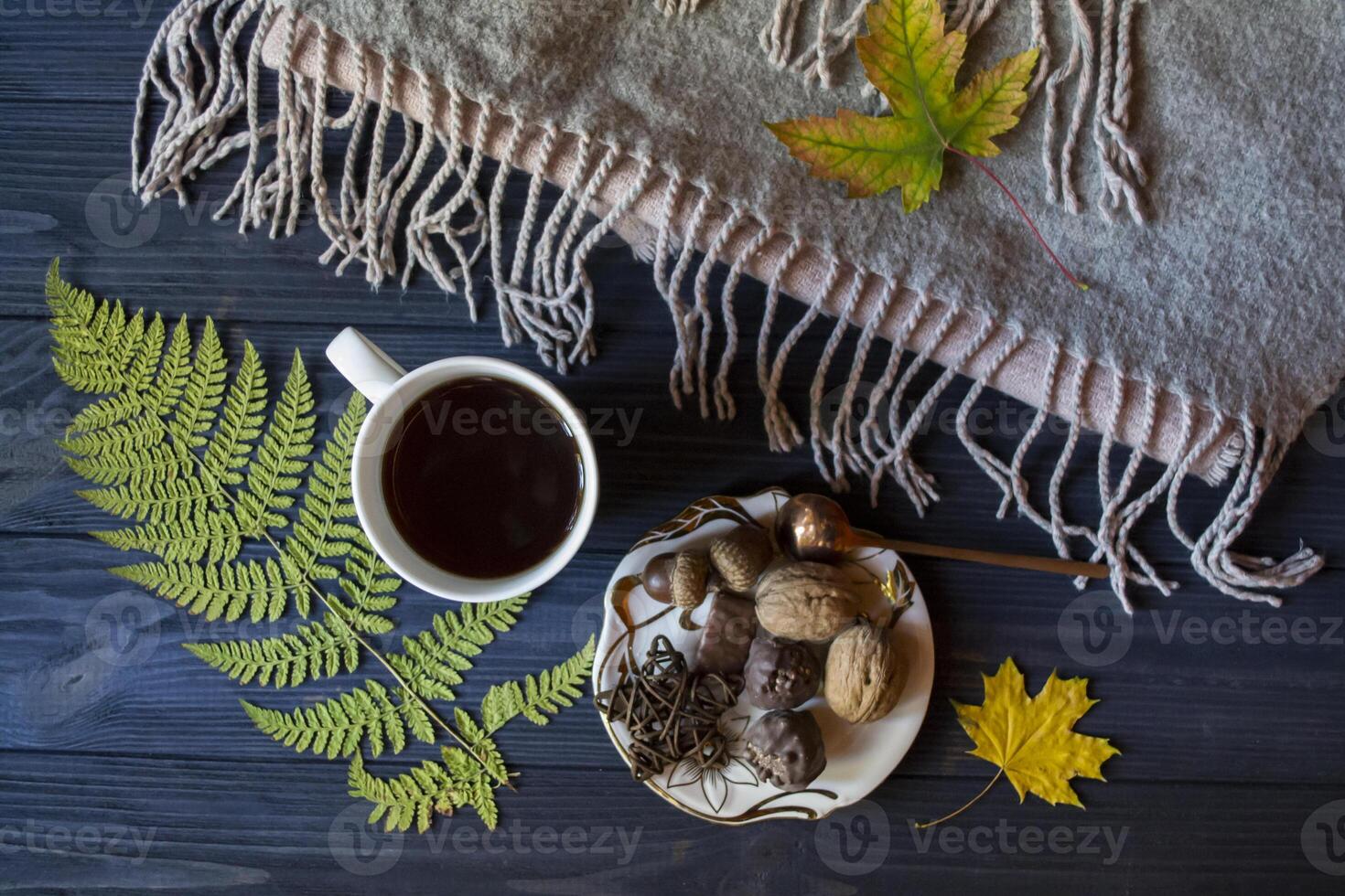 A cup of tea and sweet snacks with decoration by autumn leaves on the warm plaid. Seasonal still life photo