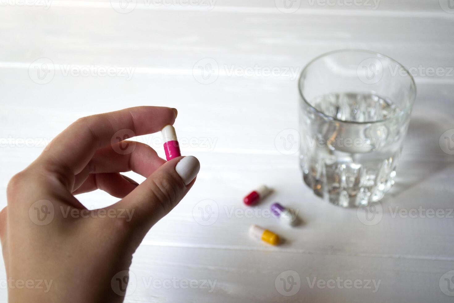 A capsule in female hand and glass of water on a white table. photo