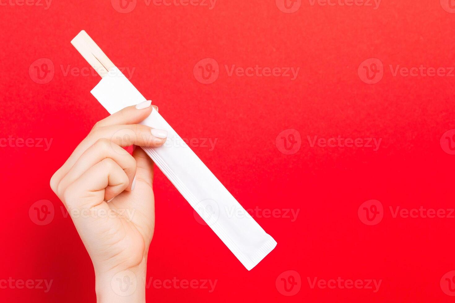 mano de mujer sosteniendo palillos en un paquete sobre fondo rojo. concepto de comida china con espacio vacío para tu diseño foto