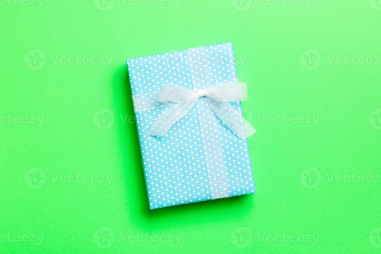 wrapped Christmas or other holiday handmade present in paper with white ribbon on green background. Present box, decoration of gift on colored table, top view with copy space photo
