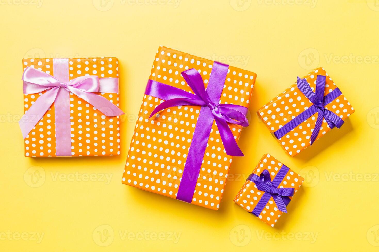 wrapped Christmas or other holiday handmade present in paper with purple and pink ribbon on yellow background. Present box, decoration of gift on colored table, top view photo