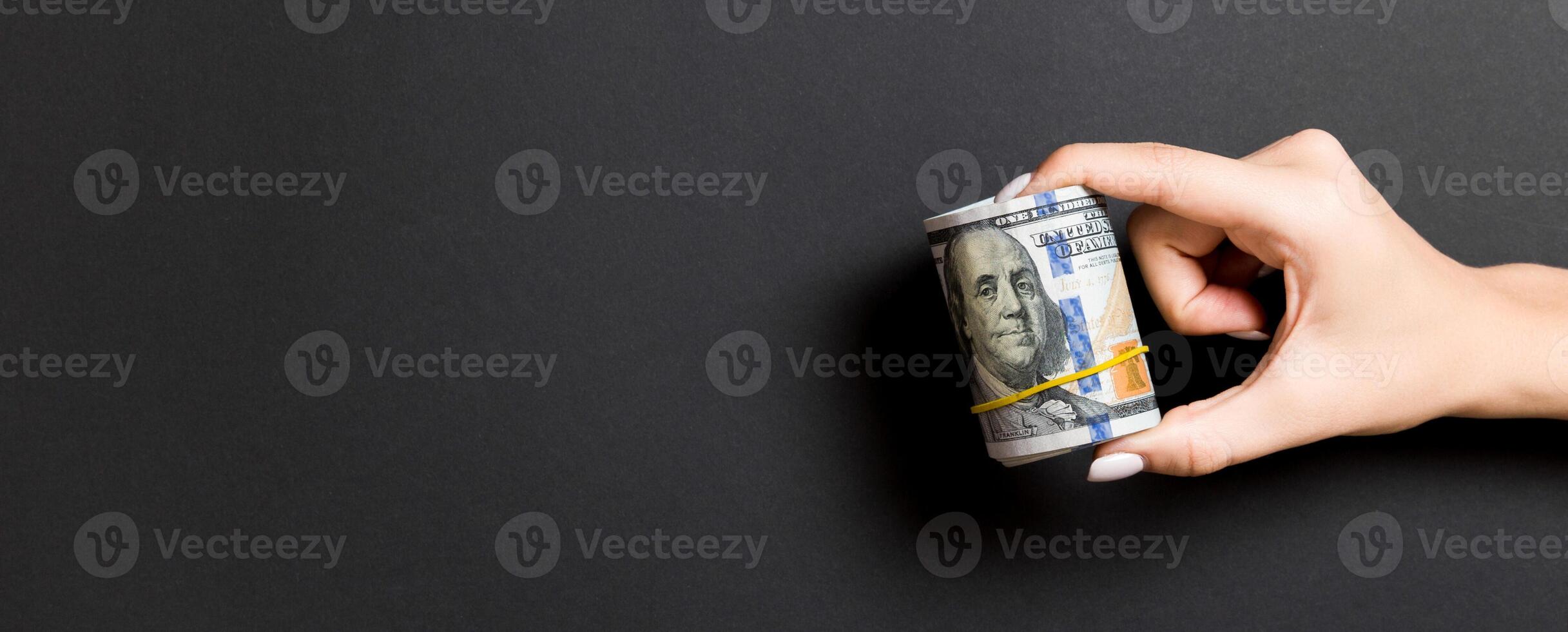 A pack of rolled one hundred dollar bills in female hand on colorful background. Salary concept with copy space photo