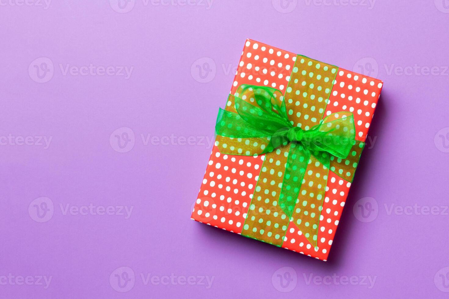 wrapped Christmas or other holiday handmade present in paper with green ribbon on purple background. Present box, decoration of gift on colored table, top view with copy space photo