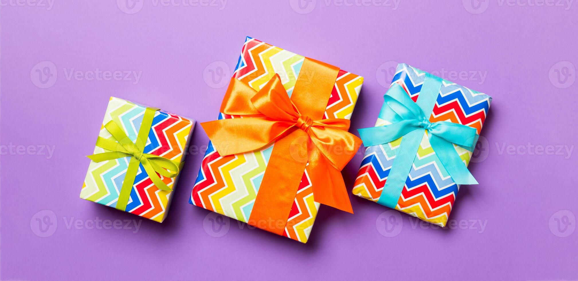 wrapped Christmas or other holiday handmade present in paper with blue, green and orange ribbon on purple background. Present box, decoration of gift on colored table, top view photo