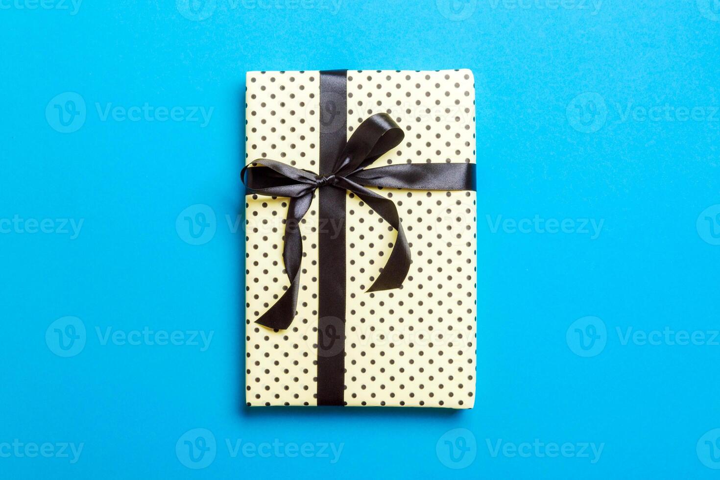 wrapped Christmas or other holiday handmade present in paper with black ribbon on blue background. Present box, decoration of gift on colored table, top view with copy space photo