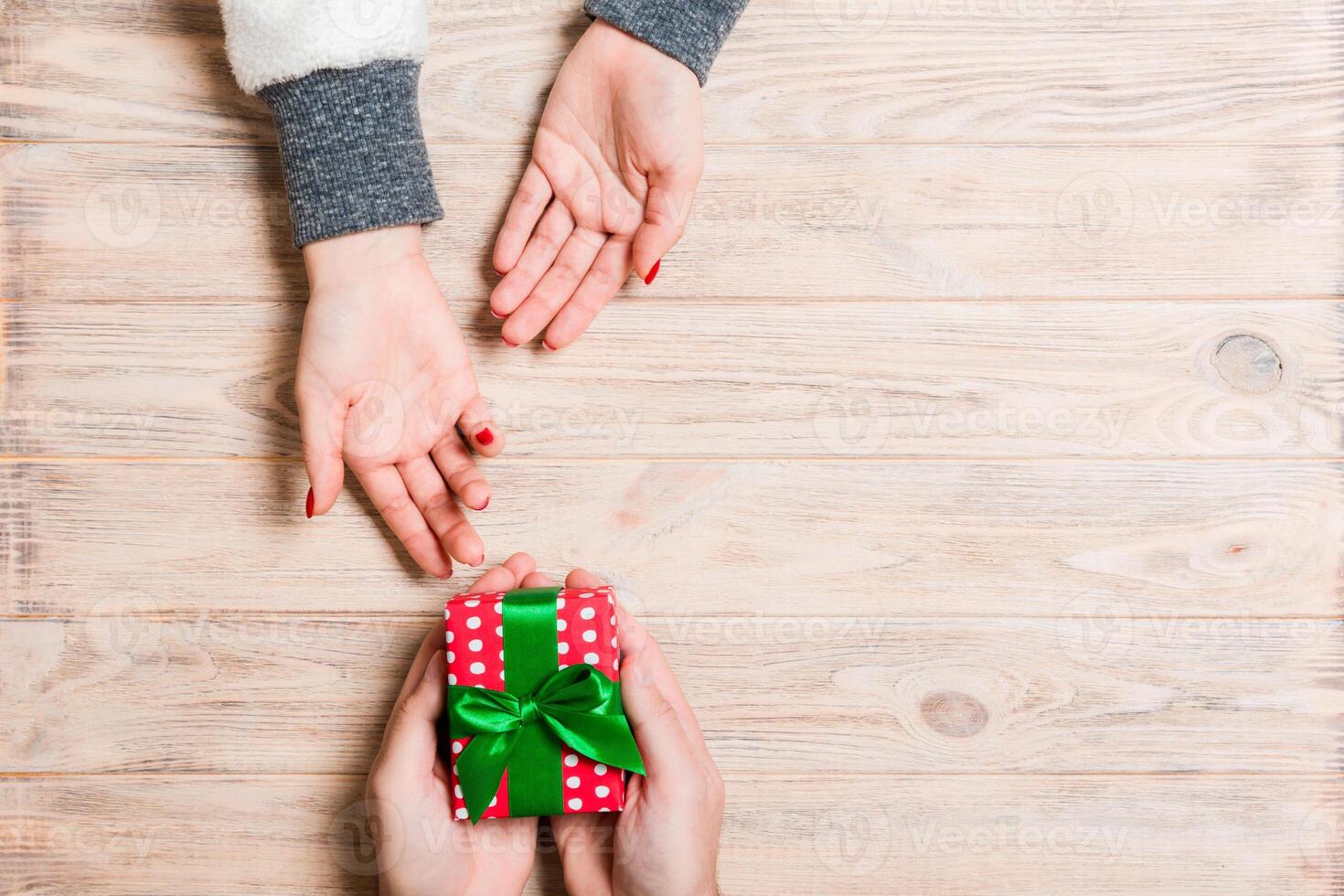 Top view of two people sharing a present on wooden background. Holiday and surprise concept. Copy space photo