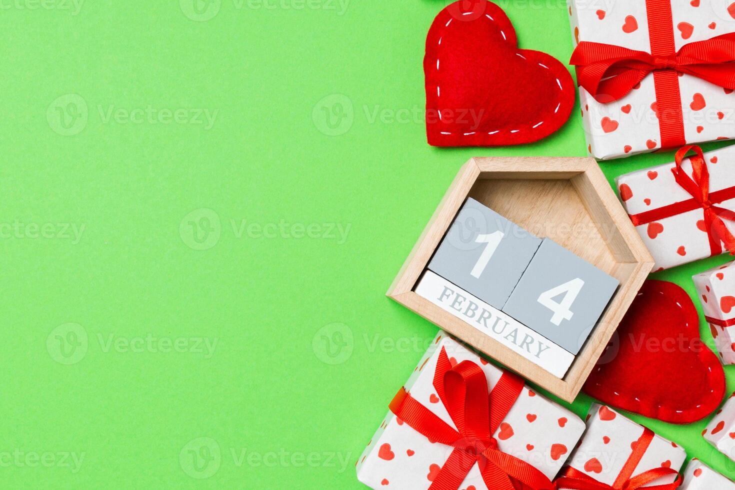 Holiday composition of gift boxes, wooden calendar and red textile hearts on colorful background with empty space for your design. The fourteenth of February. Top view of Valentine's Day concept photo
