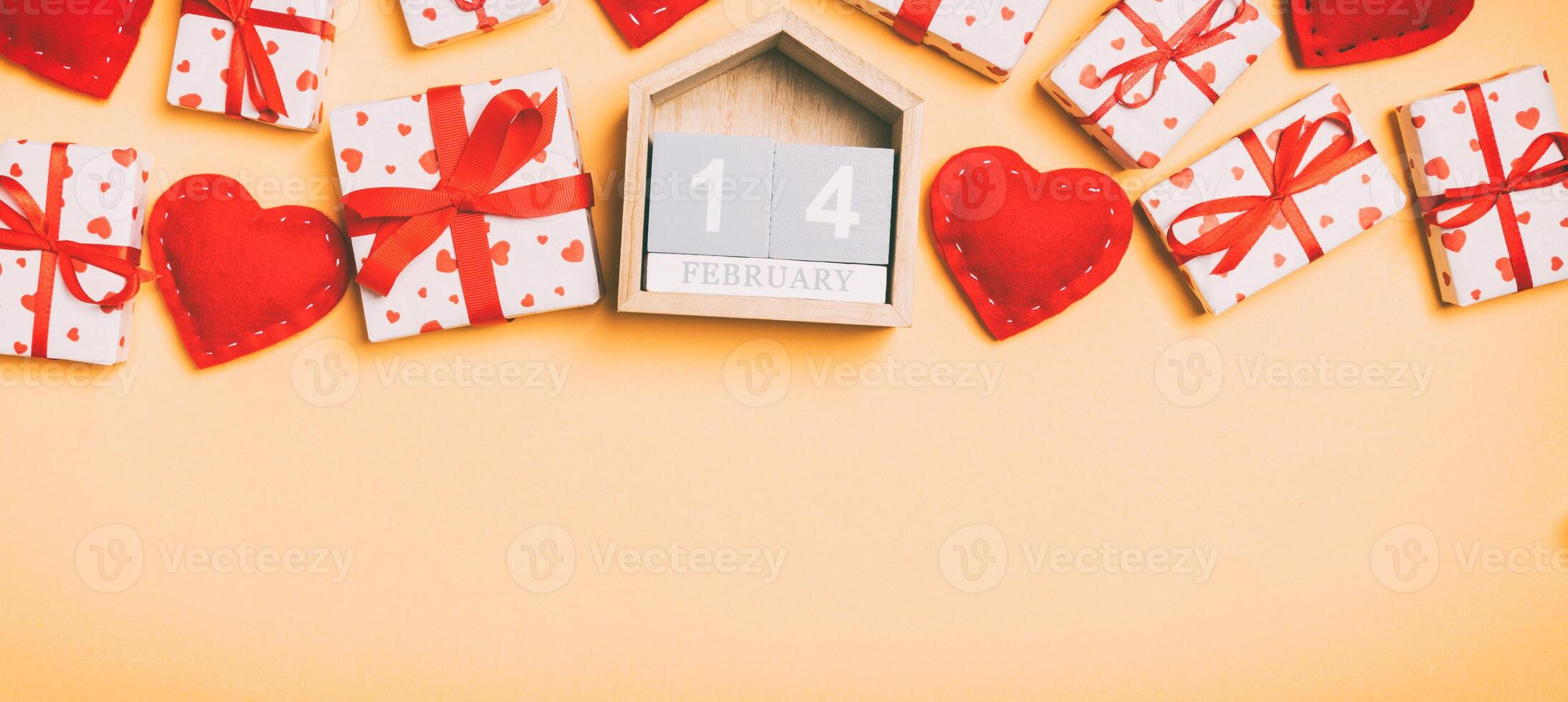 Top view of gift boxes, wooden calendar and red textile hearts on colorful background. The fourteenth of february. St Valentine's day concept with copy space photo