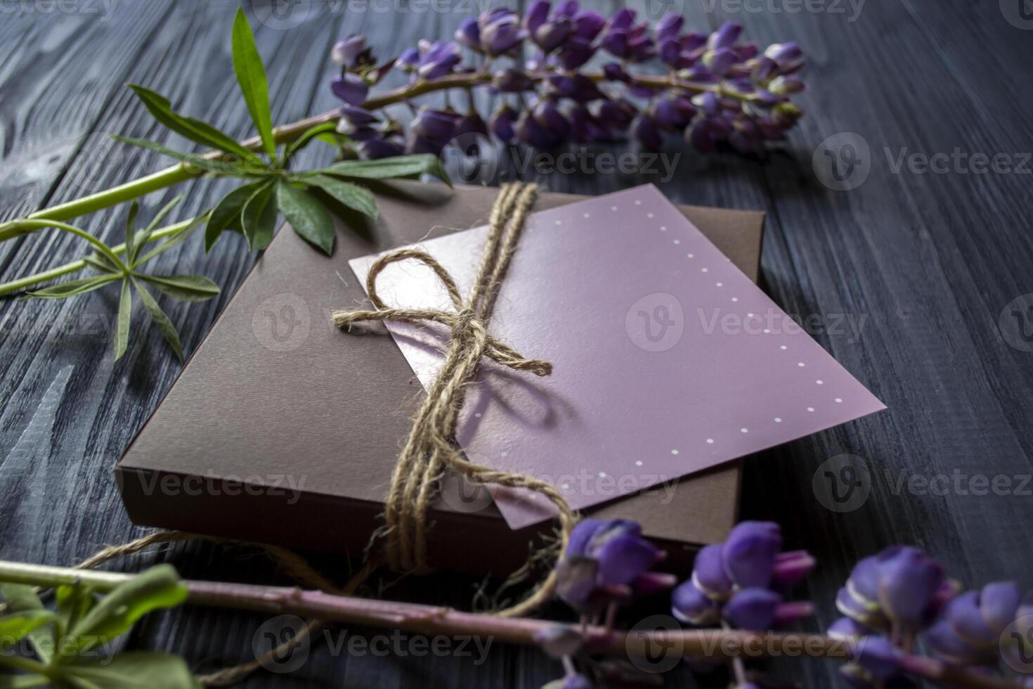 Gift box with greeting card and bouquet of lupins on a dark blue wooden background. photo