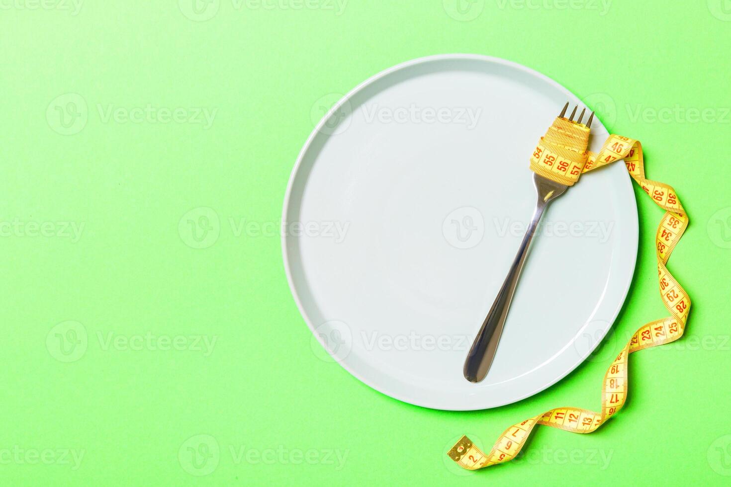 Strict diet concept with empty space fro your design. Top view of plate with fork in measuring tape on green background photo