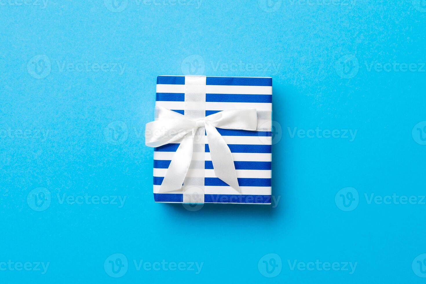 Gift box with white bow for Christmas or New Year day on blue background, top view with copy space photo