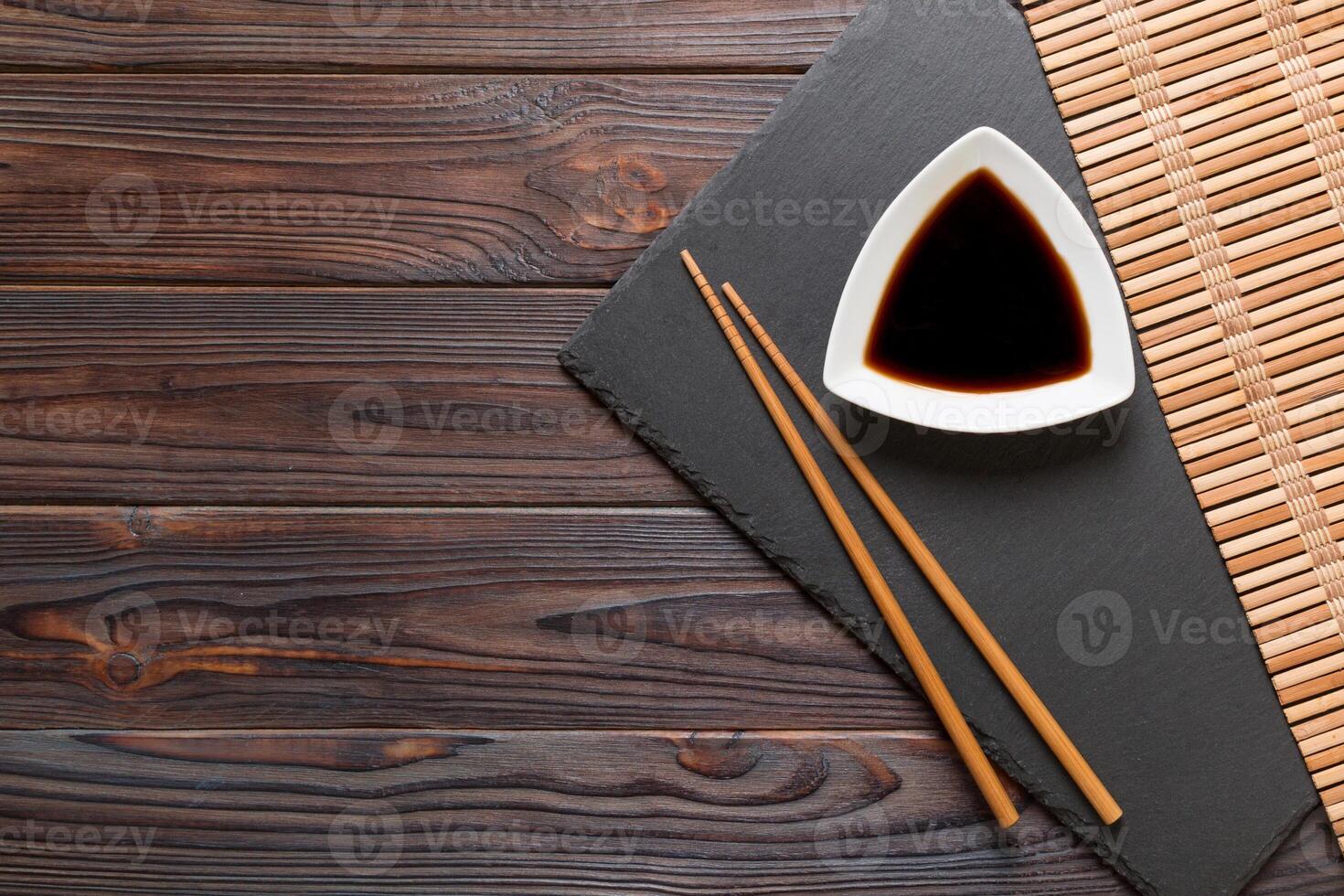 Chopsticks and soy sauce on black stone plate, wooden background with copy space photo