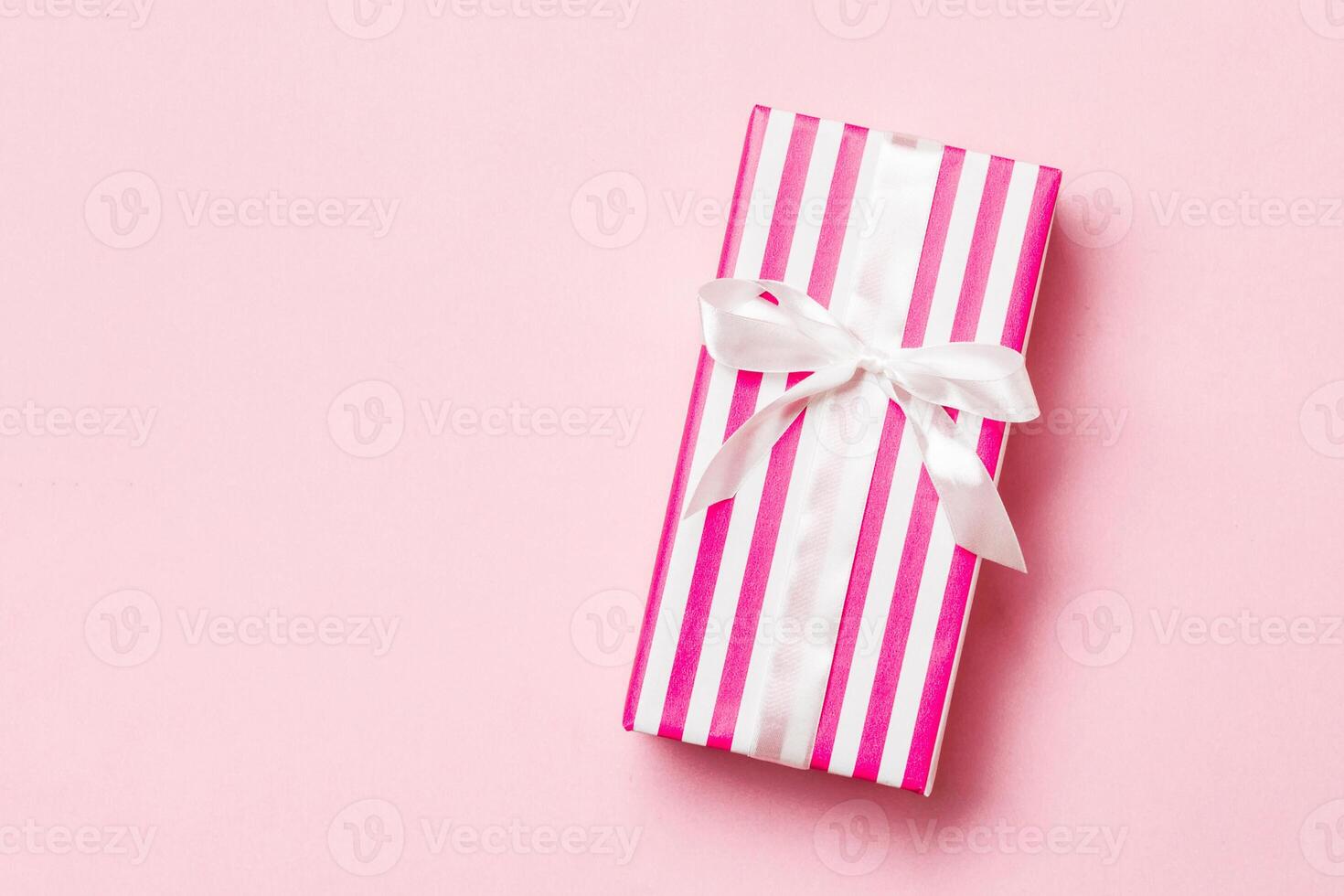 envuelto Navidad o otro fiesta hecho a mano presente en papel con blanco cinta en rosado antecedentes. presente caja, decoración de regalo en de colores mesa, parte superior ver con Copiar espacio foto