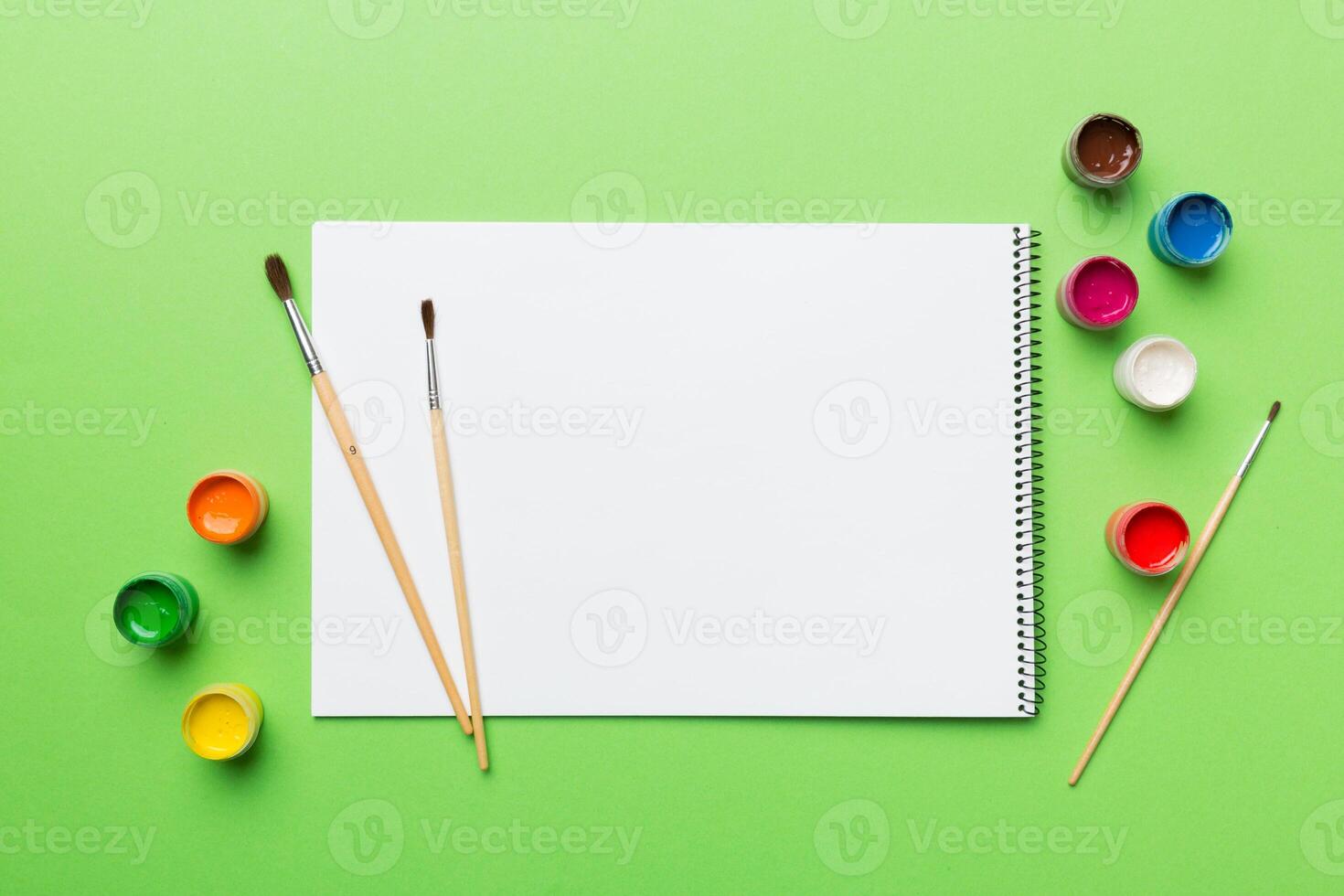 Album pages and paints, pencils, brush on a colored background. Top view with empty space. workplace for creativity. home teaching concept drawing photo