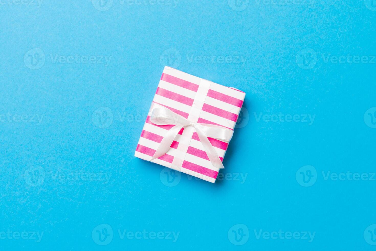 wrapped Christmas or other holiday handmade present in paper with white ribbon on blue background. Present box, decoration of gift on colored table, top view with copy space photo