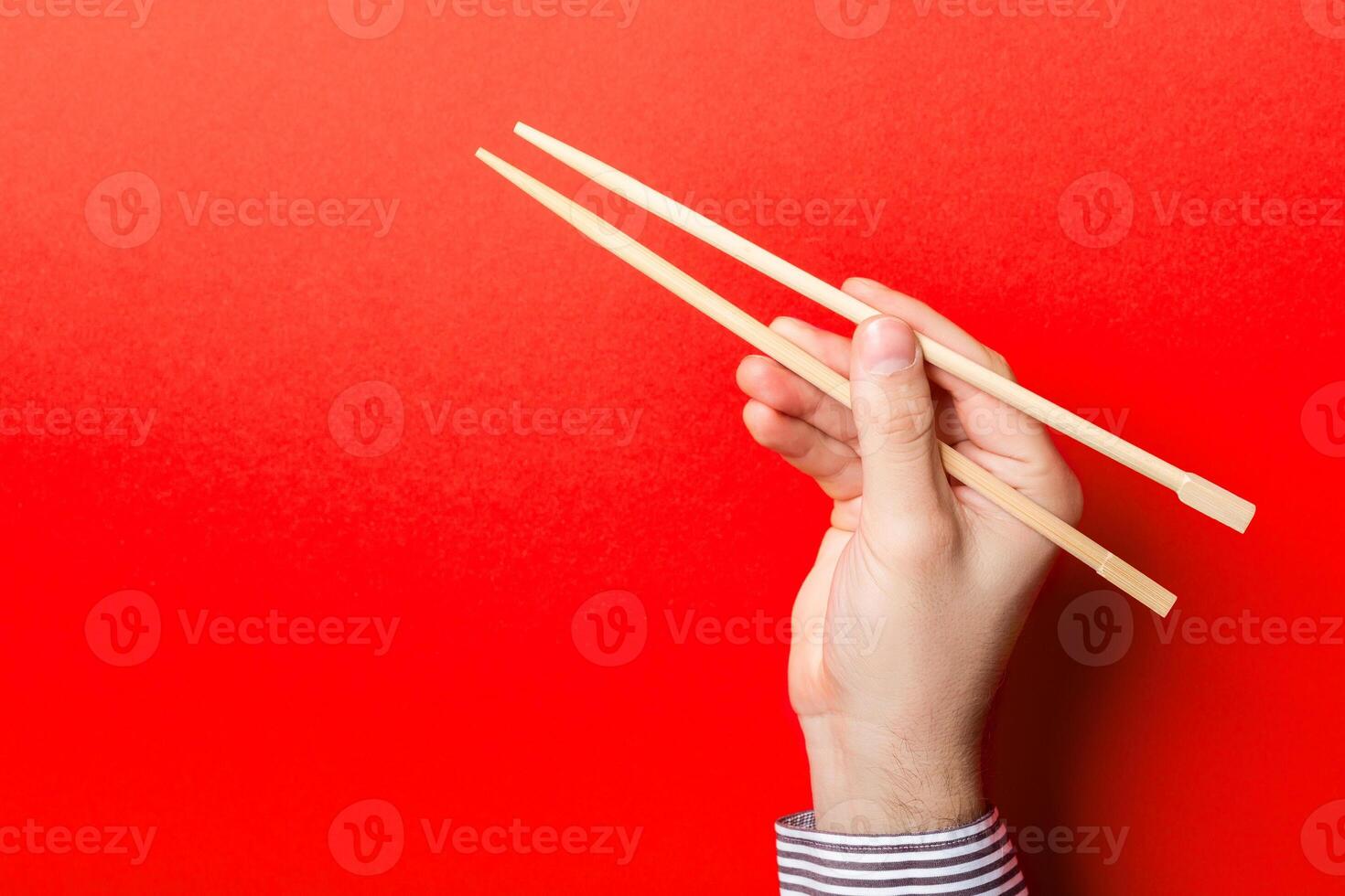 Boy's hand showing chopsticks on red background. Asian cuisine concept with empty space for your design photo