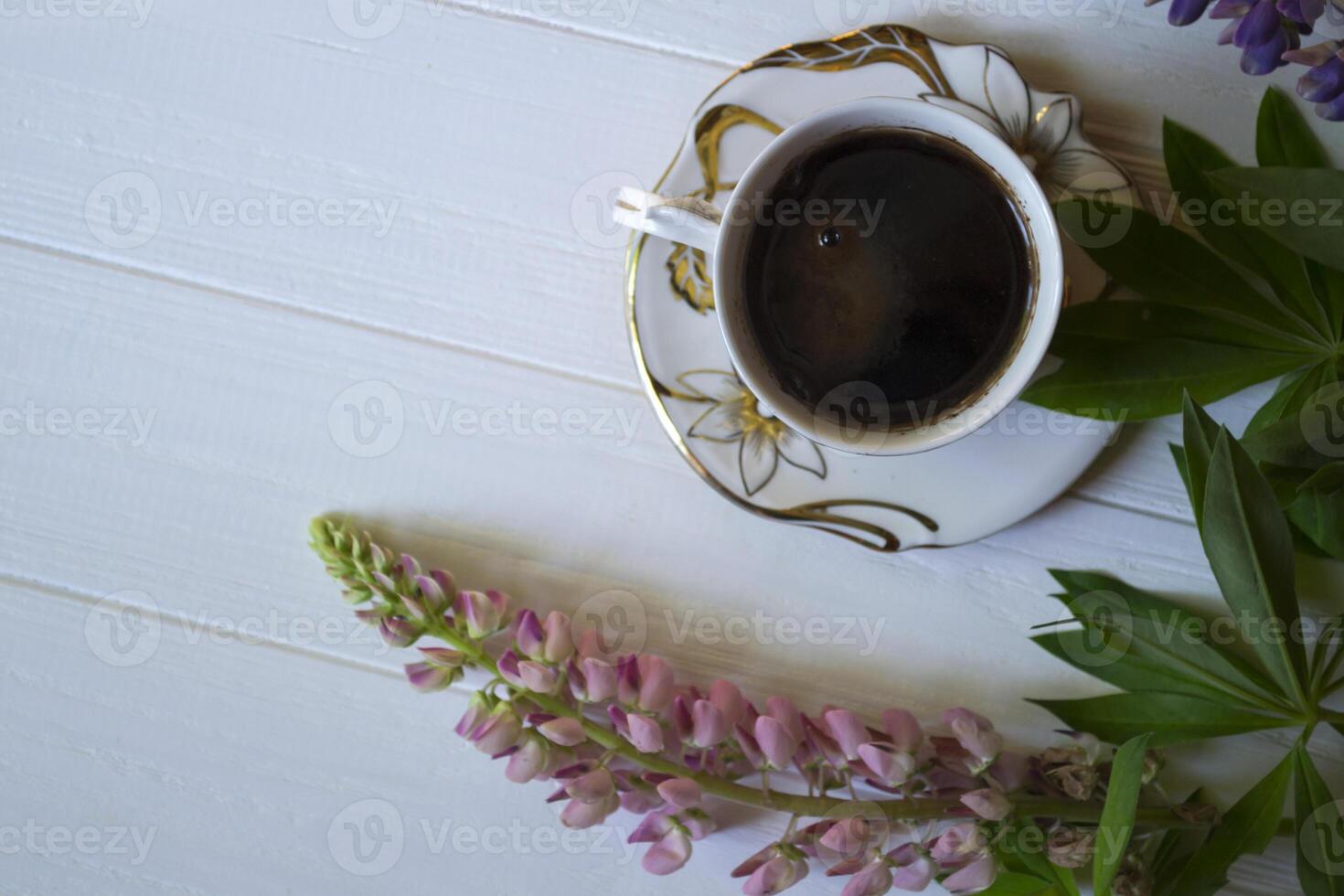 A cup of coffee and lupine flowers on a white wooden table. photo